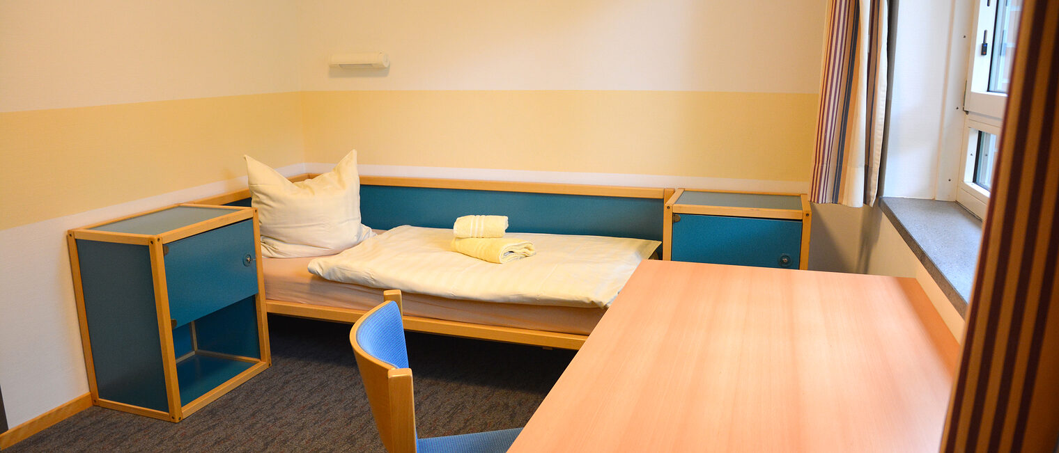 Schlafraum mit Bett, Nachtisch, Schreibtisch und einem Stuhl. 