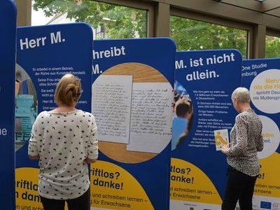 Besucher betrachten Ausstellung zur Alphabetisierung Erwachsener