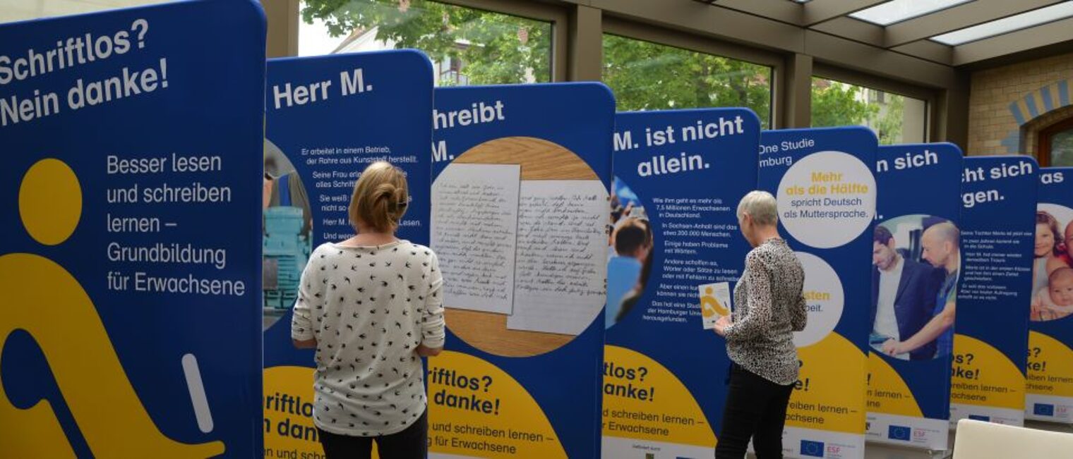 Besucher informieren sich in der Ausstellung "Schriftlos? Nein danke!" zum Thema Alphabetisierung Erwachsener. Besucher betrachten Ausstellung zur Alphabetisierung Erwachsener