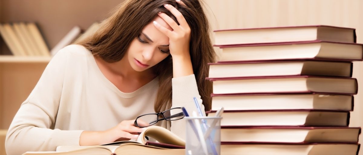 Verzweifelte Studentin vor Bücherstapel