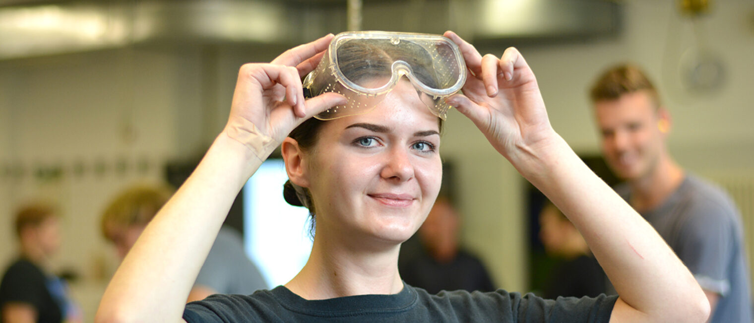 Eine Person hält ihre Sicherheitsbrille hoch.