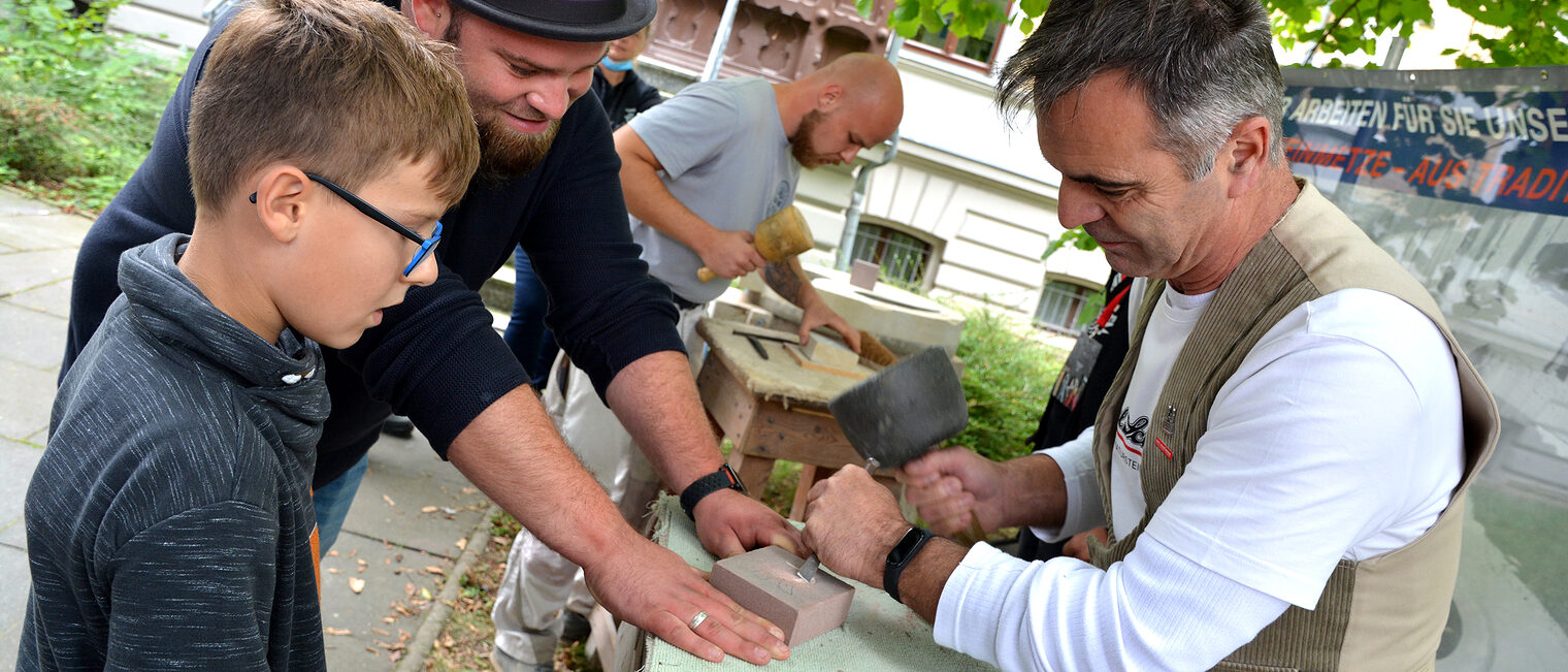 Bei Steinmetz Peter Beneke (rechts) vom Naturstein- und Baubetrieb Paul Schuster GmbH Magdeburg konnten die Besucher sich den Anfangsbuchstaben ihres Namens in Stein mei&szlig;eln lassen.