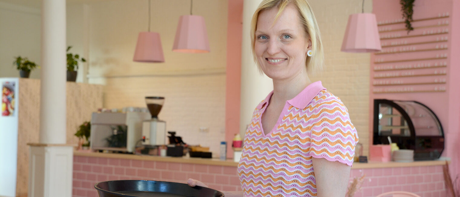 Konditorin steht in ihrem Frühstückscafé und hält eine Tasse Kaffee in der Hand.