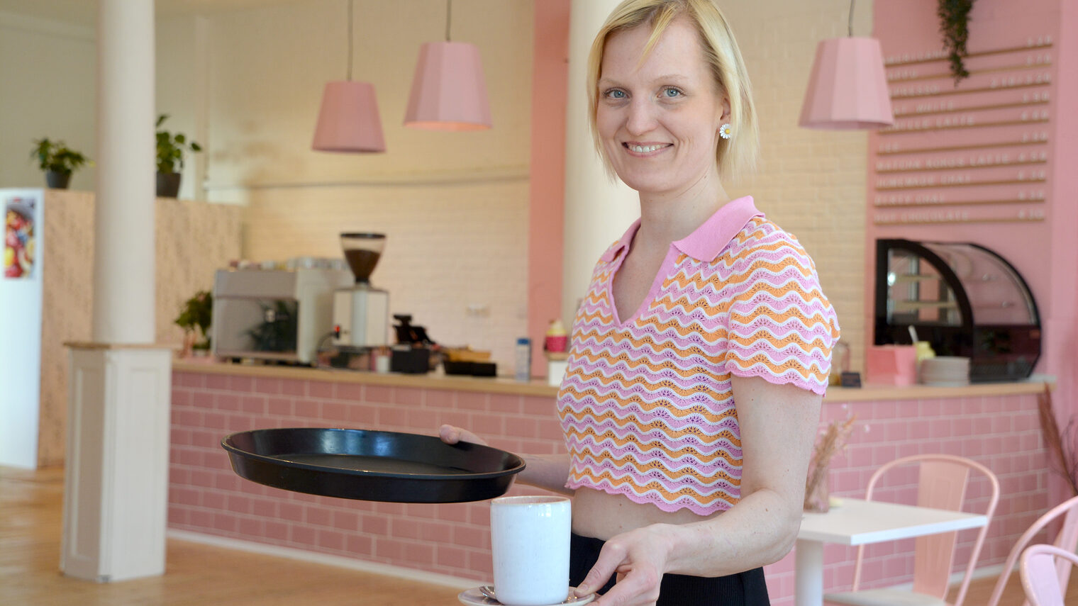 Konditorin steht in ihrem Frühstückscafé und hält eine Tasse Kaffee in der Hand.