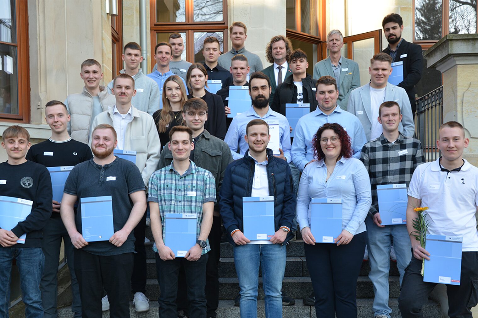 Eine Gruppe an Handwerkerinnen und Handwerker stehen vor der Handwerkskammer Magdeburg und halten ihre Gesellenbriefe in den Händen.