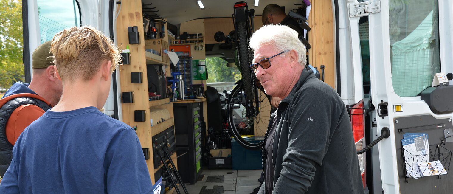 Ein Handwerker zeigt zwei Schülern seine mobile Fahrradwerkstatt.